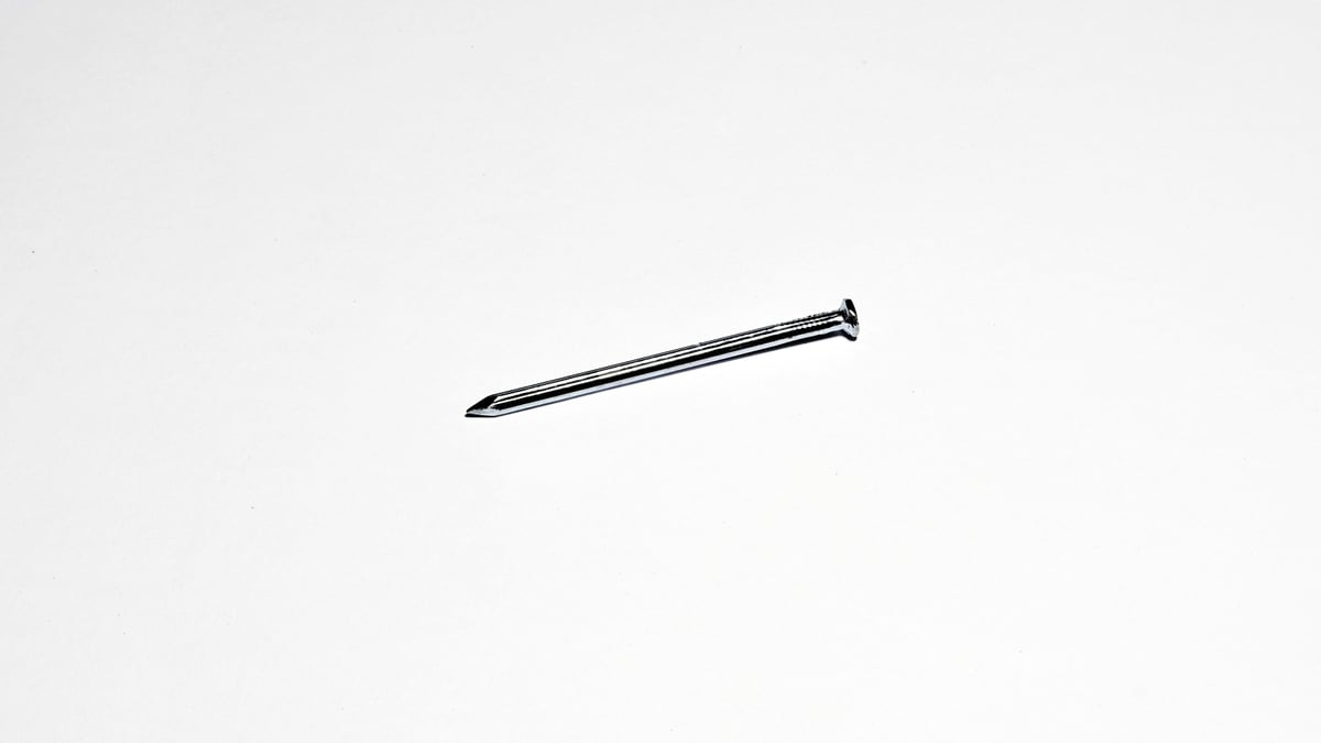 One metallic nail placed on a plain white surface.